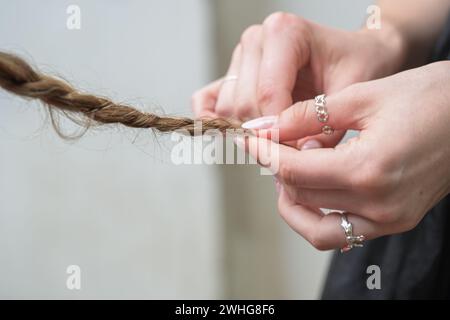 Mains d'une jeune femme avec des bagues et des ongles stylés tressant les cheveux d'un ami, espace de copie, focus sélectionné Banque D'Images