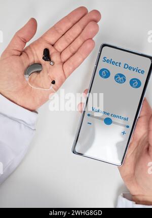 médecin audiologiste montrant l'application smartphone pour ajuster les aides auditives tenant le smartphone dans une main et les aides auditives dans l'autre. Gérer le kit de prothèses auditives Banque D'Images