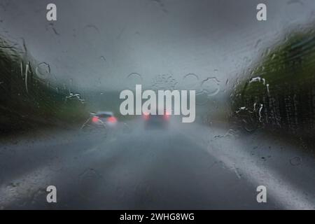 Pluie abondante sur l'autoroute, chutes épaisses sur le pare-brise et voitures floues avec des feux arrière rouges sur la route sombre, mauvaises herbes Banque D'Images