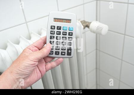 Main tenant une calculatrice devant un radiateur de chauffage plus ancien, crises d'énergie augmentant le prix du gaz et du pétrole, espace de copie, s. Banque D'Images