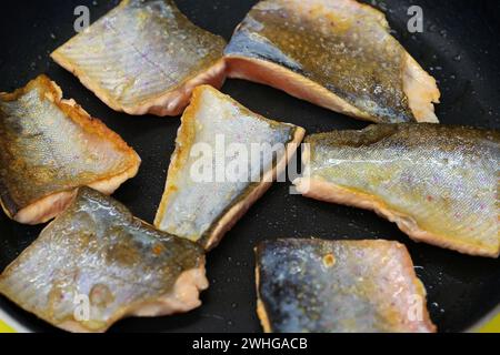 Filets de poisson de char frits sur la peau et juste retournés dans une poêle noire, cuisson d'aliments délicieux et sains, vue en angle élevé Banque D'Images