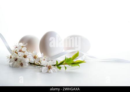 Trois œufs de Pâques blancs avec une petite branche de fleurs de fruits sauvages sur un fond clair avec espace de copie, focus sélectionné, étroit Banque D'Images