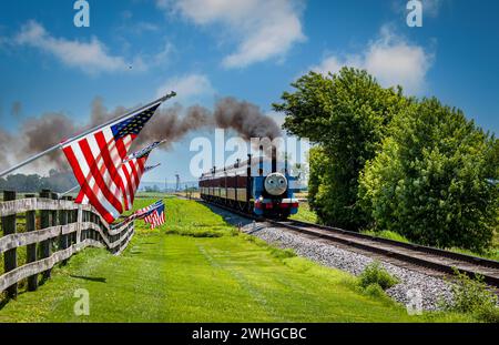 Vue de Thomas le train tirant des voitures de passagers en passant devant American Flags sur une clôture Banque D'Images