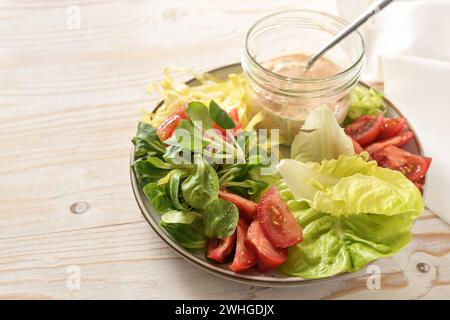 Salade fraîche de diverses laitues et tomates avec vinaigrette Thousand Island dans un bocal en verre sur une assiette et sur un woo peint en blanc Banque D'Images
