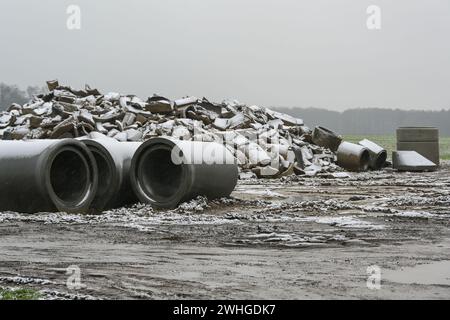 Tuyaux en béton cassés et neufs pour l'installation de drainage sur un chantier de construction dans le champ par une journée humide et enneigée Banque D'Images