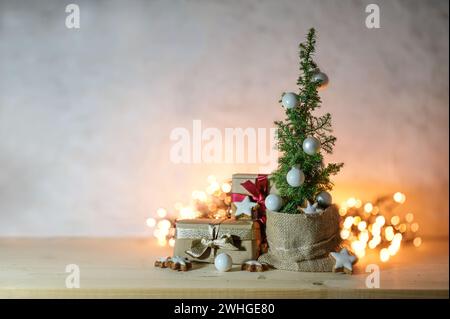 Arbre de Noël alternatif peu encombrant, petite plante de conifère en pot, décorée de boules, étoiles et cadeaux devant flou Banque D'Images