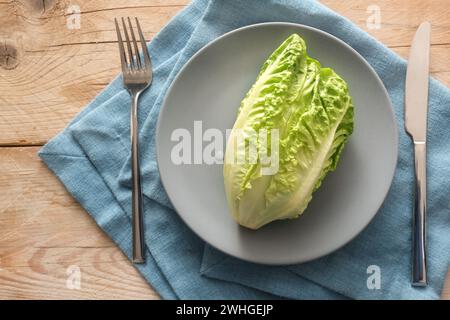 Laitue verte fraîche ou bébé cos sur une assiette grise avec des couverts sur une serviette bleue et des planches de bois rustiques, concept pour une ve saine Banque D'Images