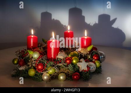 Couronne de l'Avent avec boules de Noël rouges et vertes, quatre bougies allumées et une ombre sur le mur, espace de copie, foyer sélectionné Banque D'Images