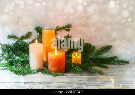 Troisième Avent, arrangement avec quatre bougies en orange et jaune, trois sont allumées avec une flamme, branches de sapin sur bois rustique clair, Banque D'Images