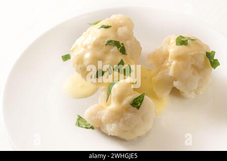 Chou-fleur cuit avec sauce hollandaise et garniture de persil sur une assiette blanche, accompagnement de légumes, espace de copie, foyer sélectionné Banque D'Images