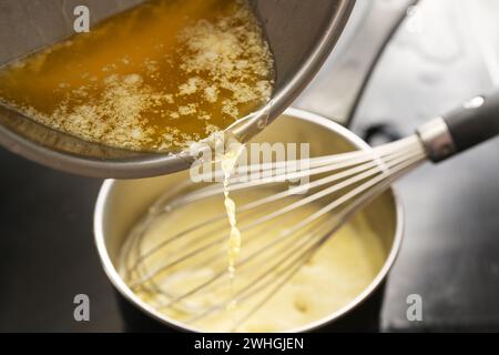 Processus de cuisson de la sauce hollandaise, verser le beurre fondu dans la casserole avec le mélange d'œufs, fouetter tout le temps à basse température Banque D'Images