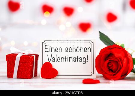 10 février 2024 : bonne Saint Valentin sur une carte de voeux à côté d'un cadeau et d'une rose rouge FOTOMONTAGE *** einen schönen Valentinstag Gruß auf einer Grußkarte neben einem Geschenk und einer roten Rose FOTOMONTAGE Banque D'Images