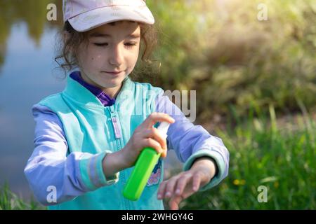 Fille pulvérise le spray moustique sur la peau dans la nature qui mordent ses mains et ses pieds. Protection contre les piqûres d'insectes, répulsif sans danger pour Banque D'Images