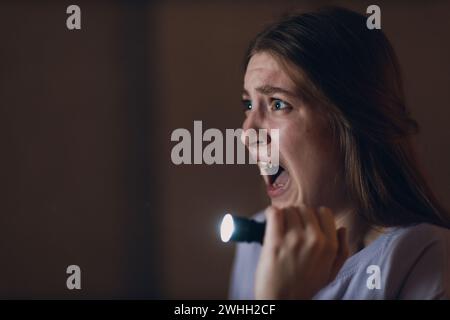 Femme effrayée tenant la main lampe de poche dans l'obscurité et peur de la violence de vol criminel. Banque D'Images