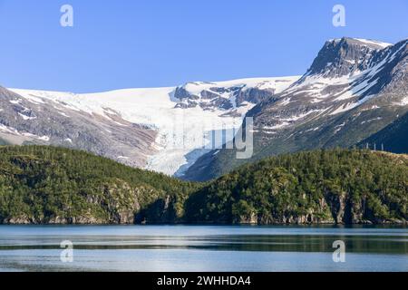 Le glacier Svartisen, drapé de blanc immaculé, se distingue des sommets accidentés, tandis que les eaux tranquilles du lac reflètent la sérénité nordique Banque D'Images