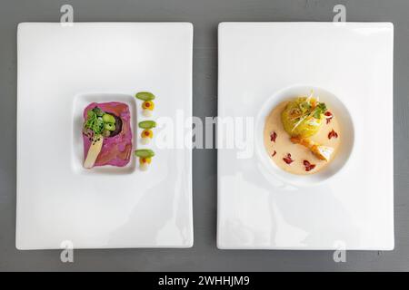 Deux plats d'un menu gastronomique moderne sur assiettes blanches, asperges à la feuille de nori avec sauce betterave, risotto safran avec crevettes et Banque D'Images