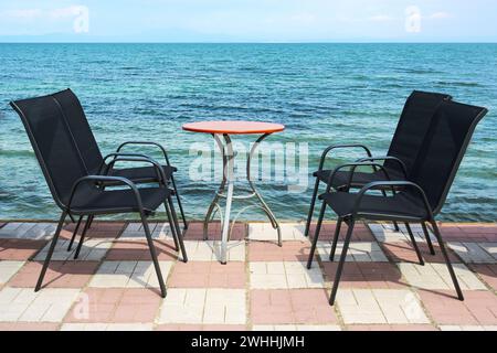 Chaises d'extérieur noires et une table de bistro ronde sur le front de mer pavé directement sur la mer Méditerranée bleue, relaxatio invitant Banque D'Images