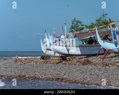 Bateau de pêche traditionnel indonésien avec stabilisateurs sur une plage de pierres à Medewi sur l'île de Bali en Indonésie. Banque D'Images