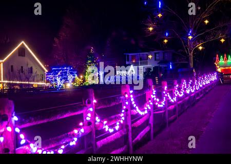 Scène de nuit d'Une rue avec des bâtiments et des arbres décorés de lumières de Noël et Une clôture en bois bordée de lumières violettes, sous Un ciel avec des lumières en forme d'étoile. Banque D'Images