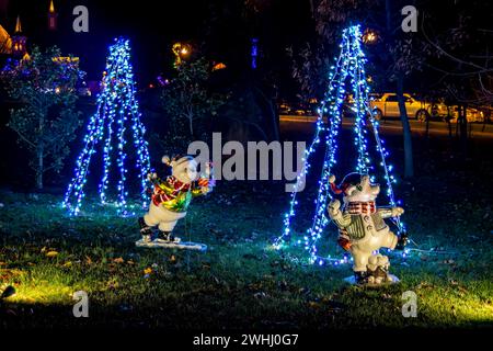 Scène nocturne d'arbres de Noël décoratifs en forme de cône éclairés avec deux figurines de bonhomme de neige gonflables ludiques au premier plan, ajoutant à la décoration extérieure festive. Banque D'Images