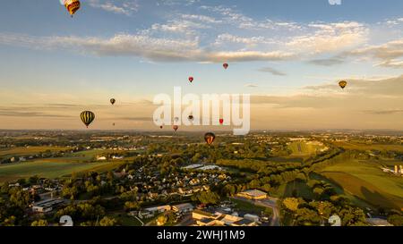 Vue aérienne du ciel ensoleillé rempli de montgolfières au-dessus d'Une ville tranquille au milieu de Green Fields lors d'un vol tôt le matin. Banque D'Images
