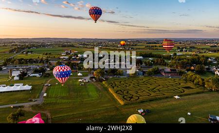 Une vue aérienne de plusieurs montgolfières survolez Un paysage pittoresque avec Un labyrinthe de maïs, une ville et des champs pendant Un coucher de soleil Golden Hour. Banque D'Images