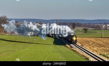 Drone vue d'un train de passagers à vapeur antique approchant voyageant à travers la campagne et les terres agricoles soufflant de la fumée Banque D'Images