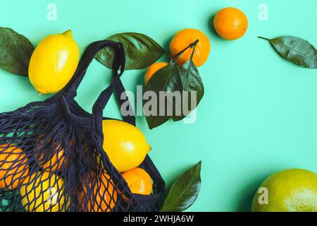 Agrumes dans un sac textile en maille sur fond de menthe. Nourriture saine et concept zéro déchet Banque D'Images