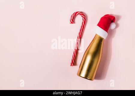 Canne de bonbons de Noël et champagne doré dans le chapeau de Père Noël sur fond rose. Concept de vacances minimal Banque D'Images