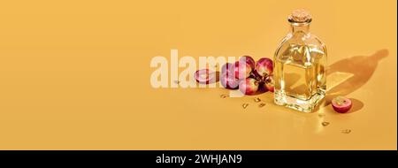 Bannière avec huile de pépins de raisin en bouteille et bouquet de raisins sur fond jaune et ombres à la mode. Réutiliser les déchets alimentaires Banque D'Images