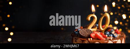 Bannière avec gâteau d'anniversaire au chocolat avec des baies, des biscuits et le numéro vingt bougies dorées sur fond noir, espace de copie Banque D'Images