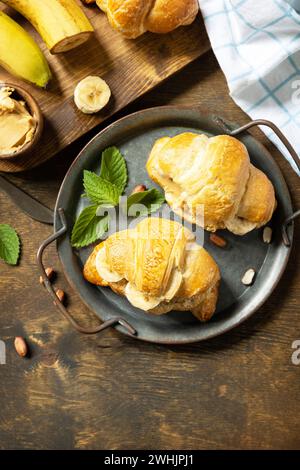 Concept de dessert alimentaire sain. Pâtisserie française. Savoureux croissants fraîchement cuits au four avec du beurre d'arachide et de la banane sur un fond rustique Banque D'Images