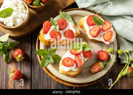 Petits pains grillés petit déjeuner, nourriture saine. Sandwich avec des fraises et du fromage à pâte molle sur fond de bois. Banque D'Images