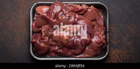 Foie de poulet cru dans le plateau de supermarché noir vue de dessus sur la table de cuisine de fond en béton rustique foncé. Ingrédient alimentaire sain, Banque D'Images