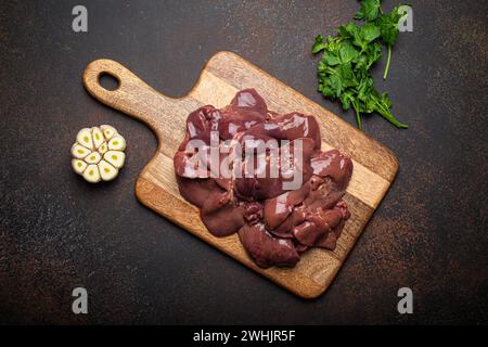 Foie de poulet cru sur planche à découper en bois vue de dessus sur fond de béton rustique foncé table de cuisine avec persil et ail. HEA Banque D'Images