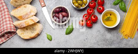 Composition alimentaire avec ciabatta tranchée, olives, huile d'olive, spaghetti, basilic frais, tomates cerises sur pierre de béton gris rustique Banque D'Images