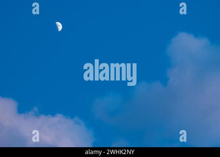 Le croissant de lune cireux est brillant dans un ciel nocturne bleu profond avec des nuages cumulus illuminés légèrement rose par le soleil, basse-Saxe, Allemagne Banque D'Images