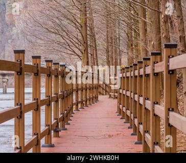 Passerelle en bois longeant la rivière recouverte d'une fine couche de glace avec un mur de montagne de granit en arrière-plan en Corée du Sud Banque D'Images