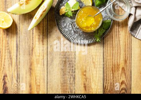 Réserve maison. Confiture ou gelée de melon sucré et d'agrumes dans un petit pot en verre avec des tranches de melon frais sur une table rustique en bois. Vue f Banque D'Images