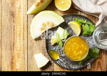 Réserve maison. Confiture ou gelée de melon sucré et d'agrumes dans un petit pot en verre avec des tranches de melon frais sur une table rustique en bois. Vue f Banque D'Images