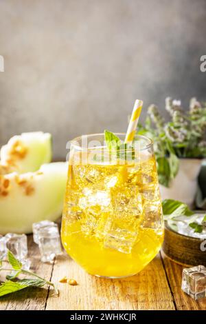 Limonade de melon dans des verres avec de la glace et de la menthe sur une table rustique en bois. Boisson d'été fruitée fraîche et rafraîchissante, boissons saisonnières. Banque D'Images