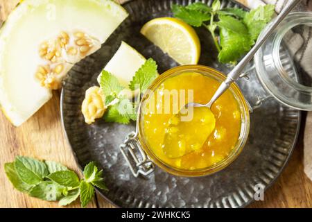 Réserve maison. Confiture ou gelée de melon sucré et d'agrumes dans un petit pot en verre avec des tranches de melon frais sur une table rustique en bois. Vue f Banque D'Images