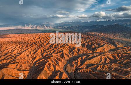 Paysage de collines érodées, badlands au coucher du soleil, sommets montagneux des montagnes Tian Shan en arrière-plan, vue aérienne, Canyon de l'oublié Banque D'Images