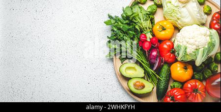 Plateau en bois rustique avec sélection de légumes frais et de verdure sur table de cuisine blanche vue dessus. Végétarien et alimentation diététique pour Banque D'Images