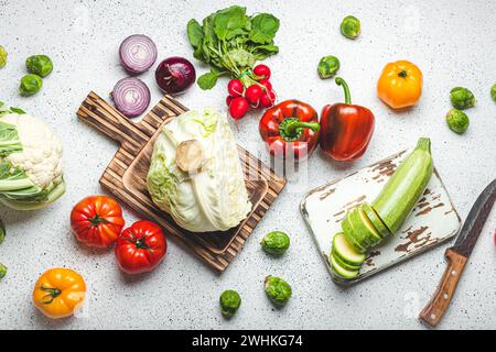 Légumes frais divers avec planches à découper en bois et couteau sur table de cuisine blanche vue de dessus. Cuisson du repas végétarien de HEAL Banque D'Images