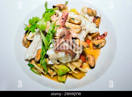 Filet de skrei norvégien rôti sur légumes colorés, avec anchois, moules, armoiries de poulpe, crevettes, coriandre fraîche et estragon, nourriture Banque D'Images