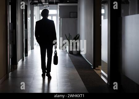 Silhouette d'un homme d'affaires en pleine hauteur, un homme à l'intérieur du bureau marche le long du couloir, des entreprises, un employé en costume d'affaires. Banque D'Images