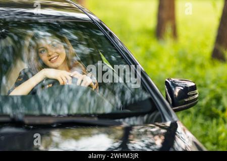 Femme heureuse conductrice à la voiture souriante. Mignonne jeune femme brune heureuse voiture de conduite. Banque D'Images