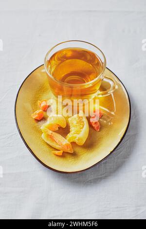 Délicieux thé noir dans une tasse en verre et fruits confits sur soucoupe jaune Banque D'Images