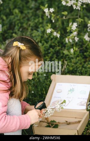 Chasse au Trésor pour les enfants dans le parc. Fille apprenant sur l'environnement. Activité d'éducation naturelle pour la Journée mondiale de la Terre. Explorer au printemps. Banque D'Images